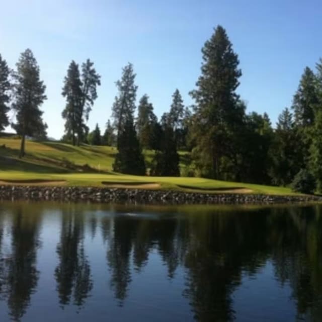 a golf course with a lake and a golf course in the foreground and trees on the other side of the lake at Kelowna Golf & Country Club in Kelowna.