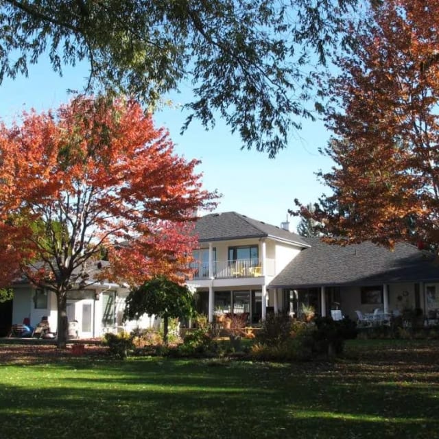 A house in the middle of a yard with trees in the foreground and grass in the foreground, Lakeshore Bed and Breakfast, Kelowna.