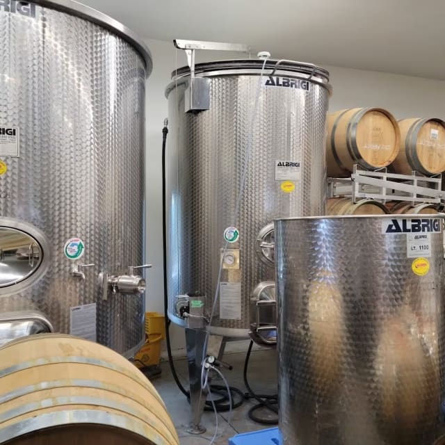 a room filled with lots of metal tanks next to wooden barrels and a wall with a clock on it.