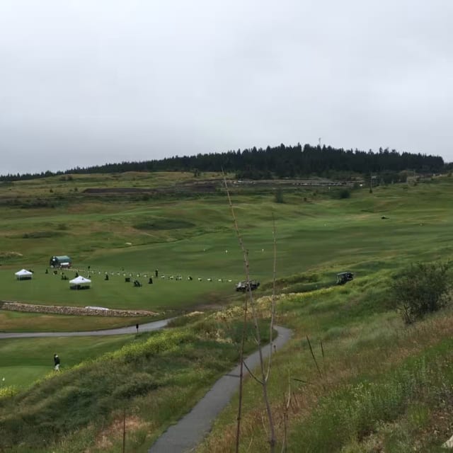 a view of a golf course from the top of a hill, with a few cars parked in the distance