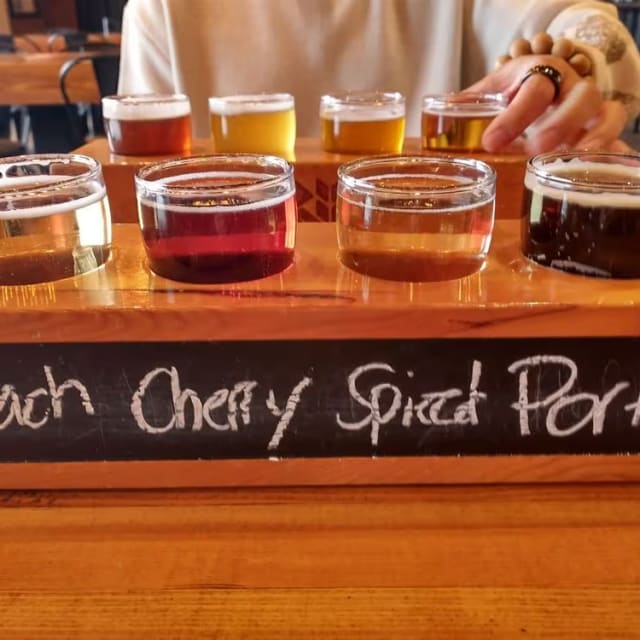 a wooden table topped with glasses filled with different types of liquid and a sign that says peach cherry spiced porter