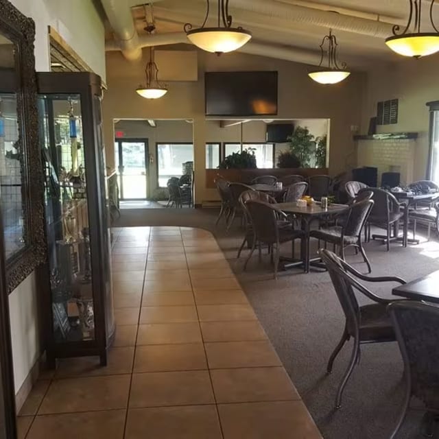 A restaurant with tables, chairs, and a display case in the middle of the room with a clock on the wall at Spallumcheen Golf & Country Club in Vernon.