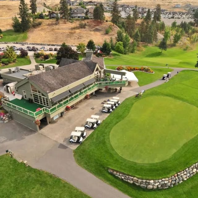 an aerial view of a golf course with cars parked in the lot and a golf club in the background
