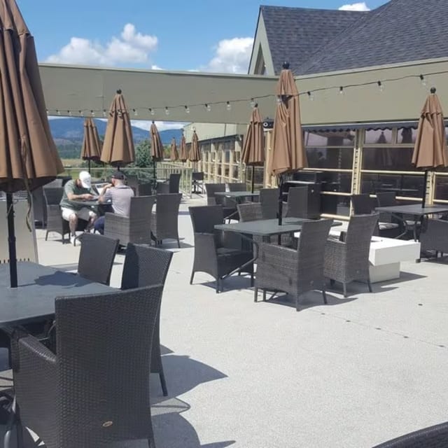 a patio with tables, chairs, and umbrellas on a patio with a view of the mountains in the distance
