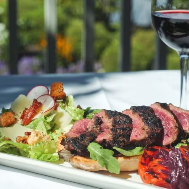 A white plate topped with meat and a salad next to a glass of red wine at The Harvest Golf Club in Kelowna.