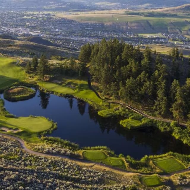 an aerial view of a golf course with a pond in the foreground and a city in the background