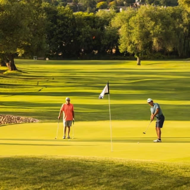 A group of people standing on top of a lush green field next to a green golf course with trees in the background.