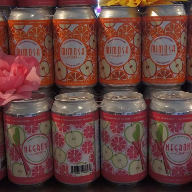 A display of Wards Cidery Mimosa and Negroni cider cans arranged in rows with pink and yellow flowers in Kelowna.