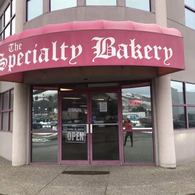 The Specialty Bakery with a pink awning located on the corner of a street in front of a building.