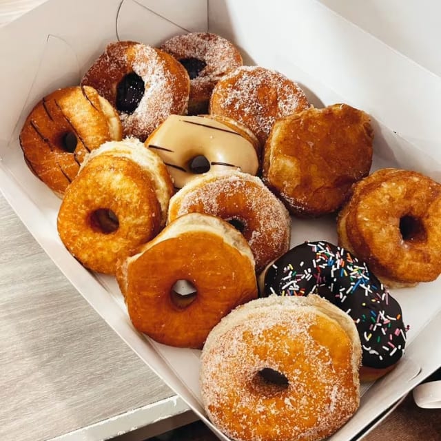 a box filled with lots of doughnuts on top of a wooden table next to a cup of coffee