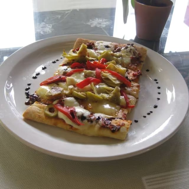 a white plate topped with a slice of pizza on top of a table next to a potted plant