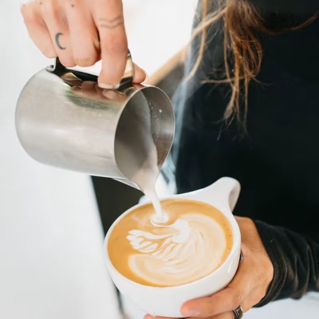 a person pouring a cup of coffee into a white cup with a white swirl on the top of it.