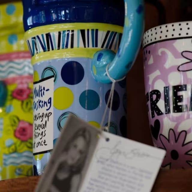 a close up of a coffee cup and a book on a table with a picture of a person on it at Marmalade Cat Cafe in Kelowna.
