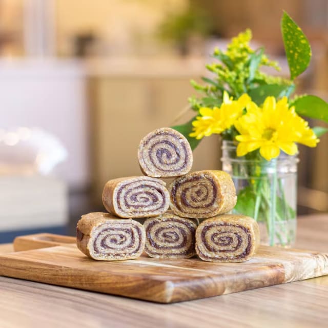 a stack of cinnamon rolls sitting on top of a wooden cutting board next to a vase with yellow flowers