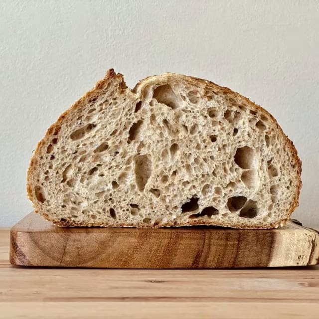 a piece of bread sitting on top of a wooden cutting board on a table next to a white wall
