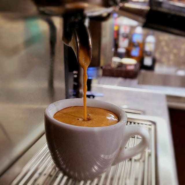 a cup of coffee being poured into a cup of coffee on top of a metal rack in a coffee shop