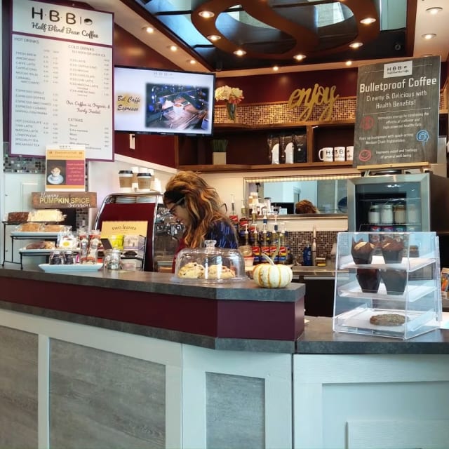 A counter in a restaurant with a lot of food on it and a menu on the wall behind it.