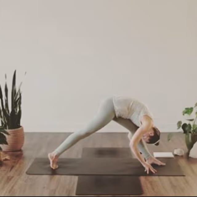 A woman practicing yoga in a serene indoor studio space with plants, a mat, and a bright, minimalist background.