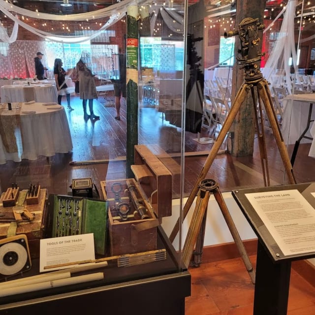 a display case with a tripod and various items on it in a room filled with tables and chairs at The Okanagan Wine & Orchard Museum in Kelowna