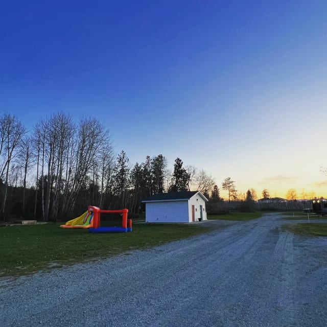 A tranquil scene at Bad Apple RV Park in Kelowna with a bounce house on a grassy field, a small white building, and a sunset sky.