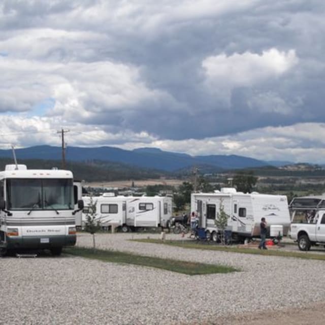 Several RVs parked at Quails View Farm & RV Park in Kelowna under a cloudy sky with mountains in the background.