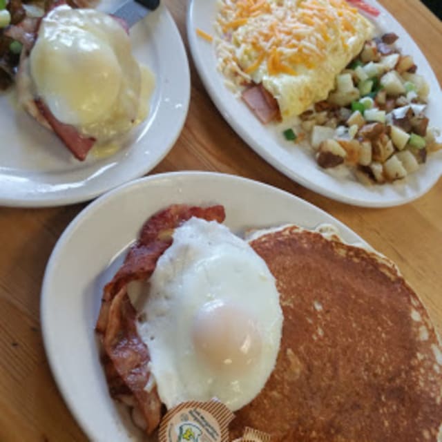 Three plates of breakfast food including eggs Benedict, an omelette with cheese and vegetables, and pancakes with bacon and eggs.