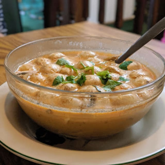 A clear glass bowl filled with a creamy Thai curry garnished with fresh cilantro, served on a white plate at Boa-Thong-Thai-Food-Restaurant in Vernon.