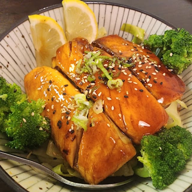 A bowl of glazed salmon fillets topped with sesame seeds and green onions, accompanied by steamed broccoli and lemon slices, at OHKIM-Sushi, Vernon, BC.
