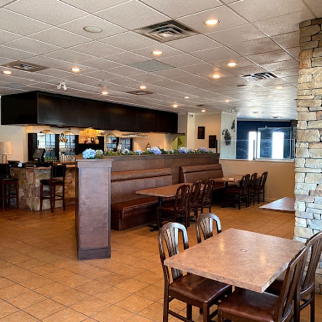 Interior of Namaste Indian restaurant in Vernon, showing dining tables, chairs, a stone wall, and a counter with decorative plants.