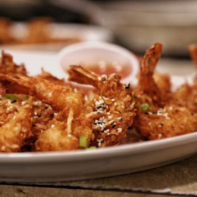 A plate of crispy fried shrimp garnished with sesame seeds and green onions, served with a dipping sauce at The Roster Sports Club Bar & Grill in Vernon.