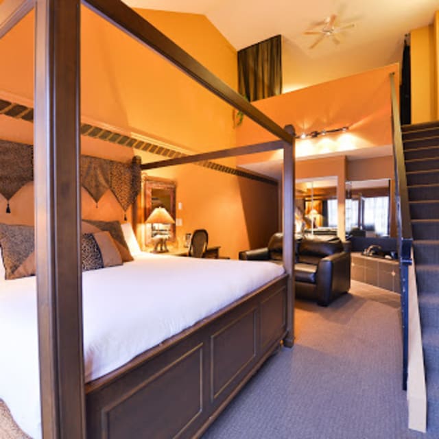 Spacious, well-lit hotel room with a four-poster bed, seating area, and stairs leading to an upper level at Prestige Hotel Vernon.