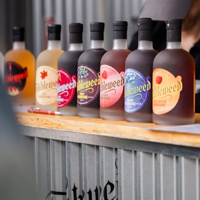 A lineup of colorful Tumbleweed spirits bottles is displayed on a wooden counter at what appears to be a distillery.
