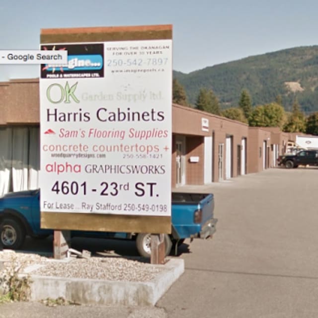 Sign for several businesses including Harris Cabinets and others at 4601 23rd St, Vernon, with view of parking lot and mountains in the background.