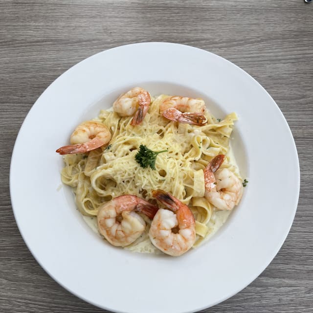 A plate of fettuccine pasta with creamy sauce and garnished with shrimp and parsley, served on a wooden table.