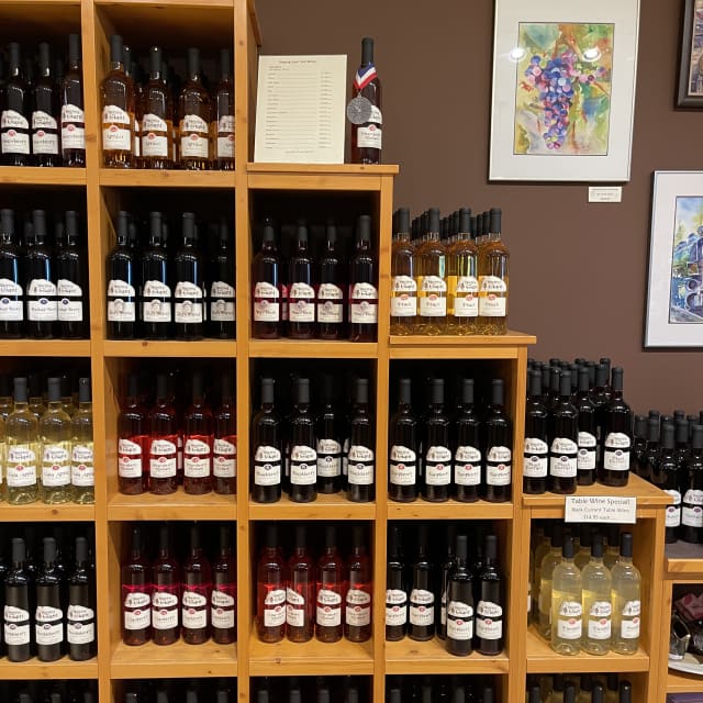 A wooden wine rack filled with various bottles of wine labeled with different fruit flavors, displayed in a store against a brown wall adorned with colorful artwork.