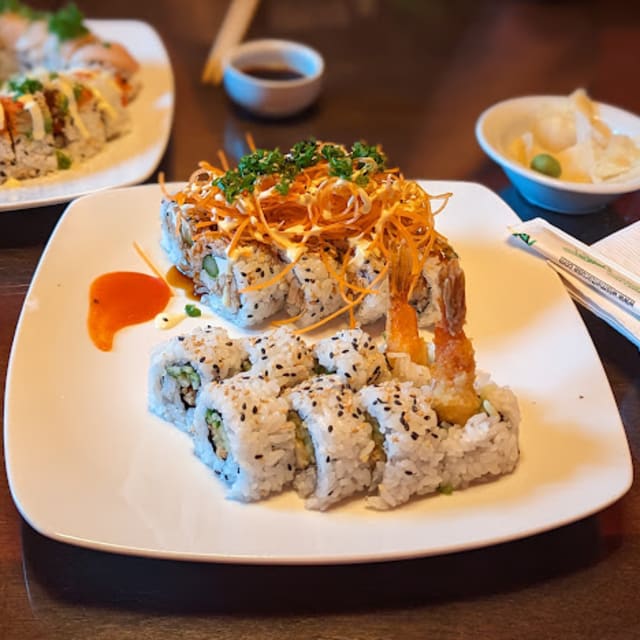 Sushi rolls topped with shredded vegetables, drizzled with sauce, and accompanied by sushi rolls with black sesame seeds at Kawakubo-Revelstoke restaurant.