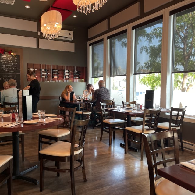 A cozy restaurant in Osoyoos with large windows, modern decor, and patrons sitting at wooden tables while a server takes an order.