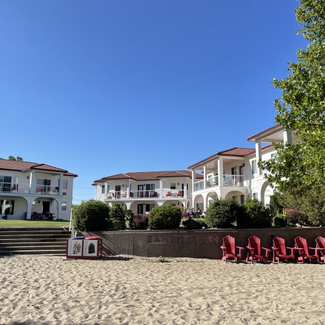 A sandy beach with red chairs in front of a resort in Osoyoos, featuring white buildings with balconies and a clear blue sky.