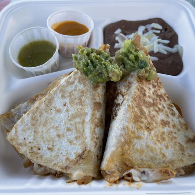 Two quesadilla slices topped with guacamole, accompanied by refried beans, green salsa, and orange salsa in a white takeaway container.