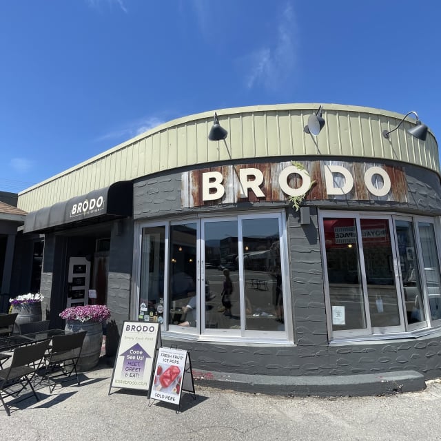 A sunny outdoor view of Brodo Kitchen & Catering in Penticton, featuring outdoor seating and promotional signs at the entrance.
