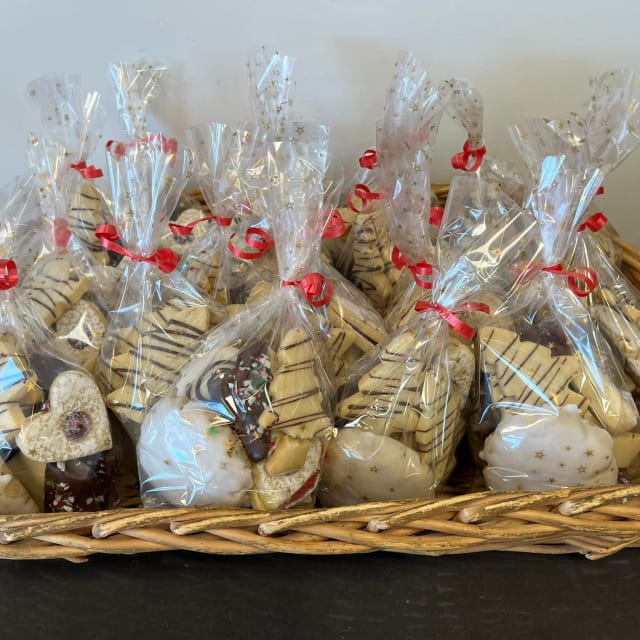 A basket filled with clear bags containing assorted cookies tied with red ribbons, displayed on a counter.