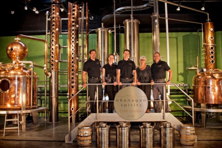 A group of people standing in front of distillation equipment at Okanagan Spirits Craft Distillery.