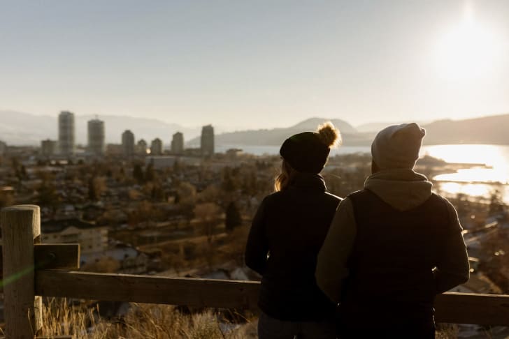 a couple of people standing next to each other on top of a wooden fence in front of a city