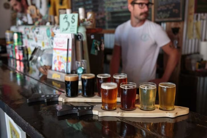 A man standing in front of a bar filled with different types of beers and a tray of beer glasses at Kettle River Brewing in Kelowna.