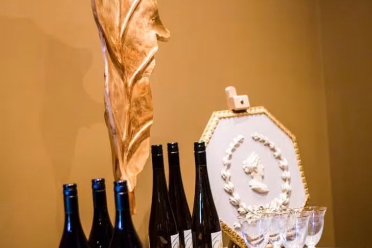 A decorated table with wine bottles, a wooden feather sculpture, and glasses at Mission Hill Family Estate Winery in West Kelowna.