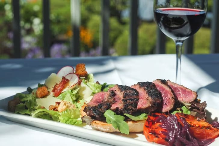 A white plate topped with meat and a salad next to a glass of red wine at The Harvest Golf Club in Kelowna.