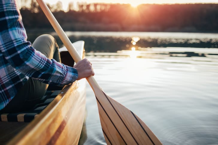 A person paddling a canoe on a lake during sunset.