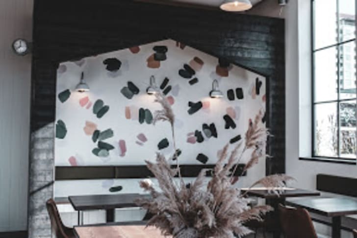 A modern cafe in Penticton with a wooden ceiling, artistic wall, large windows, and tables decorated with a vase of dried flowers.
