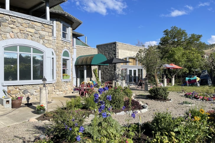 A charming stone house with arched windows and a lush garden filled with colorful flowers under a bright blue sky in Summerland.