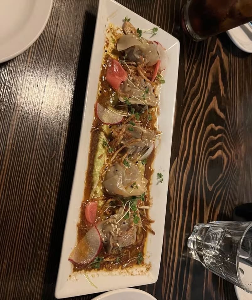 A rectangular plate with a gourmet dish featuring dumplings and garnishes, placed on a wooden table at Bernie's in Kelowna.